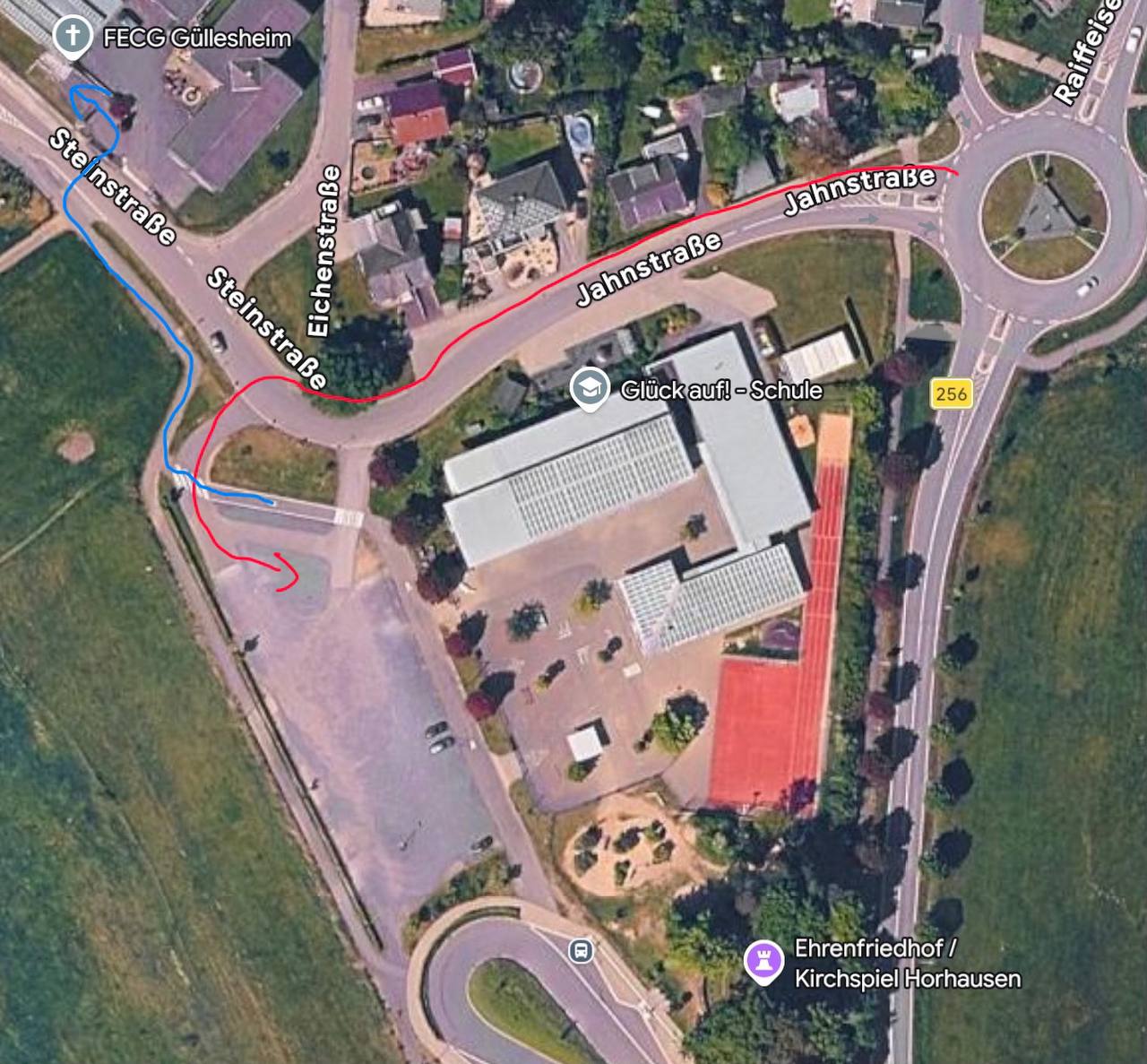 Luftbild-Lageplan: Anfahrt über die Jahnstraße vom Kreisel (B256) zum Parkplatz an der Glück-auf!-Schule (rot), von dort zu Fuß über die Steinstraße zur FECG Güllesheim (blau)